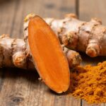 Racines de curcuma frais et poudre orange vif sur bois.